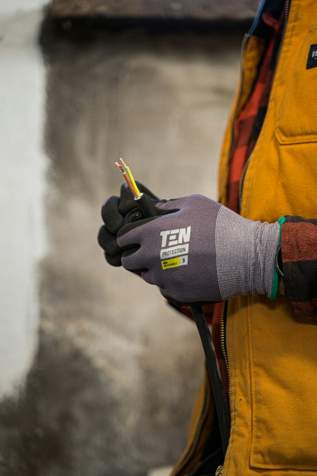 An electrician with work gloves holding a wire.